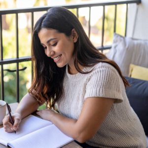 Frau sitzt am Tisch und reflektiert schriftlich ihre Woche